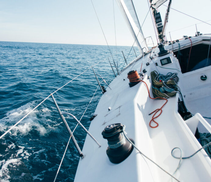 Deck of professional sailboat or racing yacht during competition on sunny and windy summer day, moving fast through waves and water, with spinnaker up, and ropes tied around winch