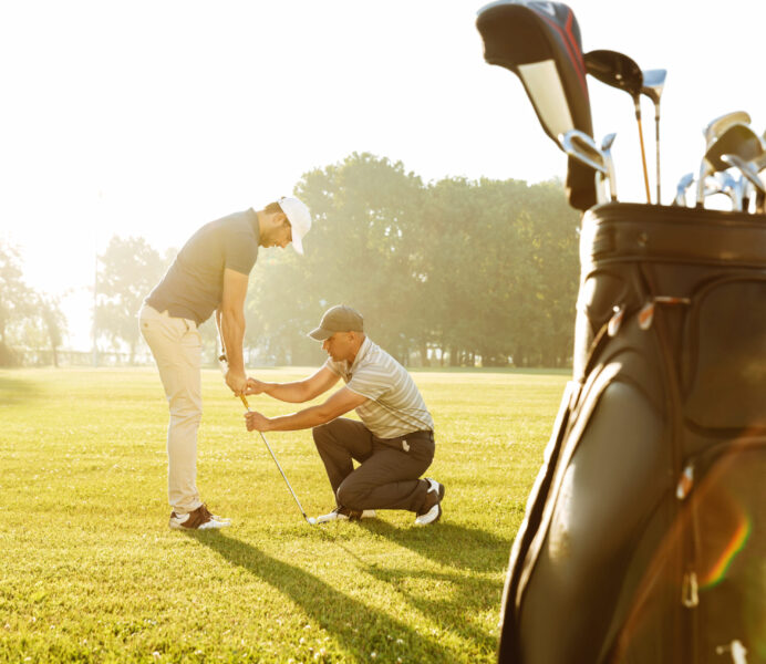 Personal trainer giving a lesson to a young male golfer while standing on a green course
